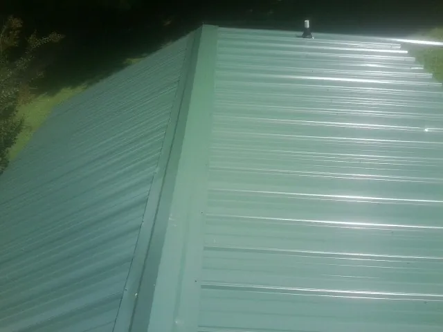 New green metal panels meeting at the ridge of a roof — Flat Roof Repair work by our crew in Clewiston